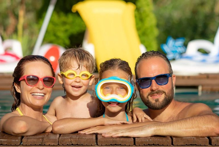 Happy family having fun on summer vacation. Father, mother and children playing in swimming pool. Active healthy lifestyle concept